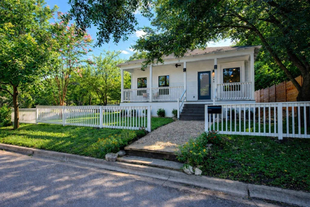 Modern white custom home exterior with covered front porch and white picket fence in Austin Texas
