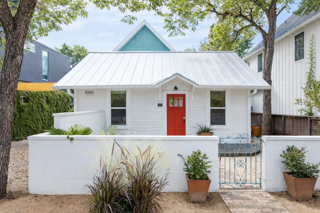 White cottage-style home with red front door and metal roof