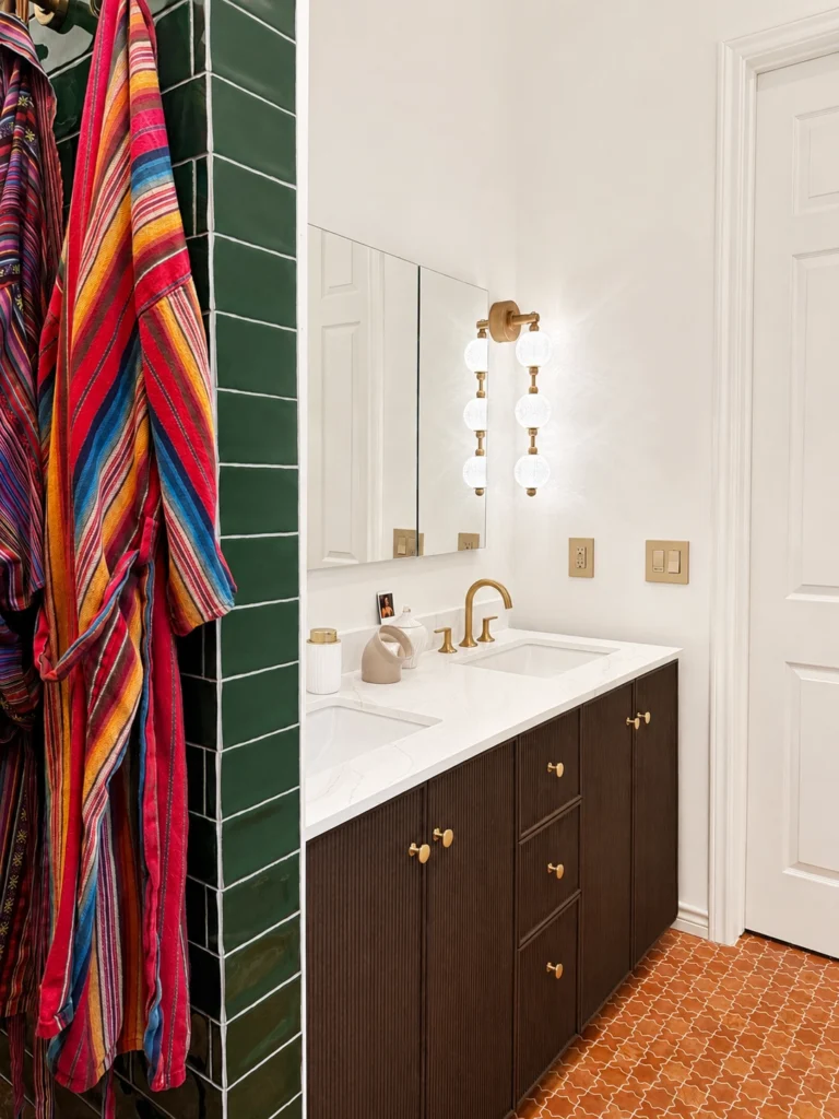 Austin bathroom remodel with green tile shower, colorful robes, dark wood double vanity, brass fixtures, and terracotta floor tile.